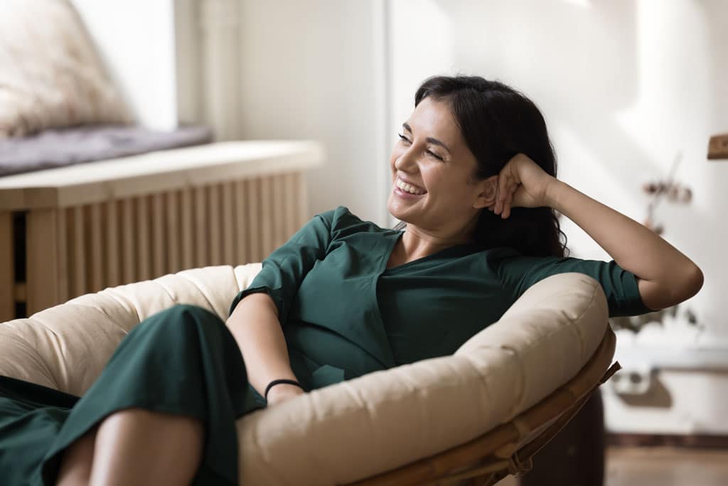 Woman wearing a green dress, smiling and relaxing in a chair in her home enjoying her AC | AC installation frisco tx dallas tx allen tx