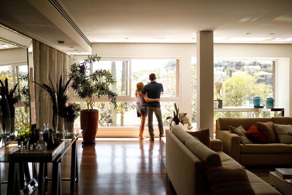 man and woman standing in front of large window of their home with lots of plants. | AC Repair Dallas, Plano, Frisco, TX