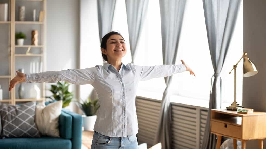 Woman standing in her home with arms wide and smiling | Humidifier services in Dallas, Frisco, and Plano, TX