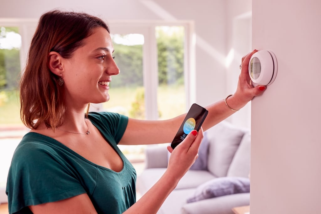 Woman adjusting her smart thermostat using her smart phone in Dallas, Highland Park, and Coppell, TX
