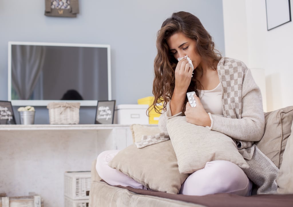 Woman sitting on a couch holding a tissue to her nose | Indoor Air Quality Services in Dallas, Frisco, and Plano, TX