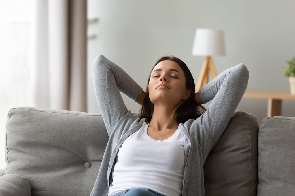 Woman sitting on her couch relaxing and leaning back with her eyes closed | Indoor Air Quality Services in Dallas, Frisco, and Plano, TX