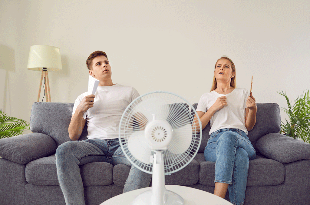young couple sitting on couch using fan to cool off heating and air conditioning service bartonville tx dallas tx allen tx 