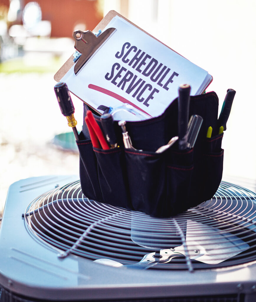 An air conditioning unit with a tool bag and a reminder sign to schedule service. Trust One Hour Air Conditioning & Heating of Dallas, TX for your residential HVAC plan. Schedule now!
