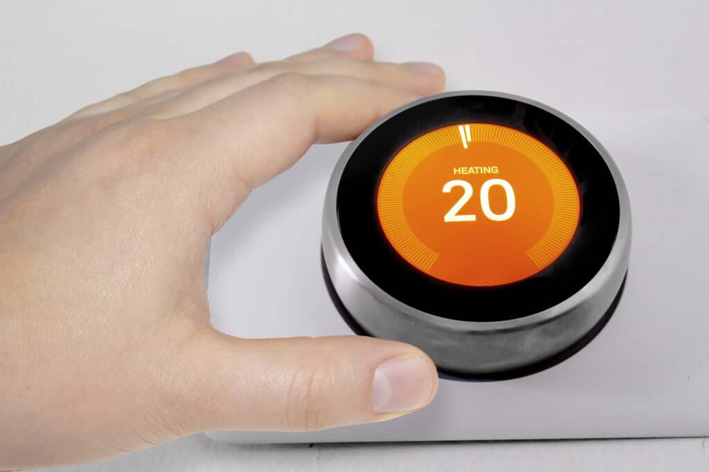 A person adjusting the temperature on a smart thermostat during winter.