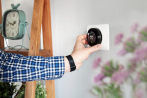 A man is adjusting the temperature on the thermostat in the living room. The thermostat is part of your HVAC system with One Hour Air Conditioning & Heating of Dallas.