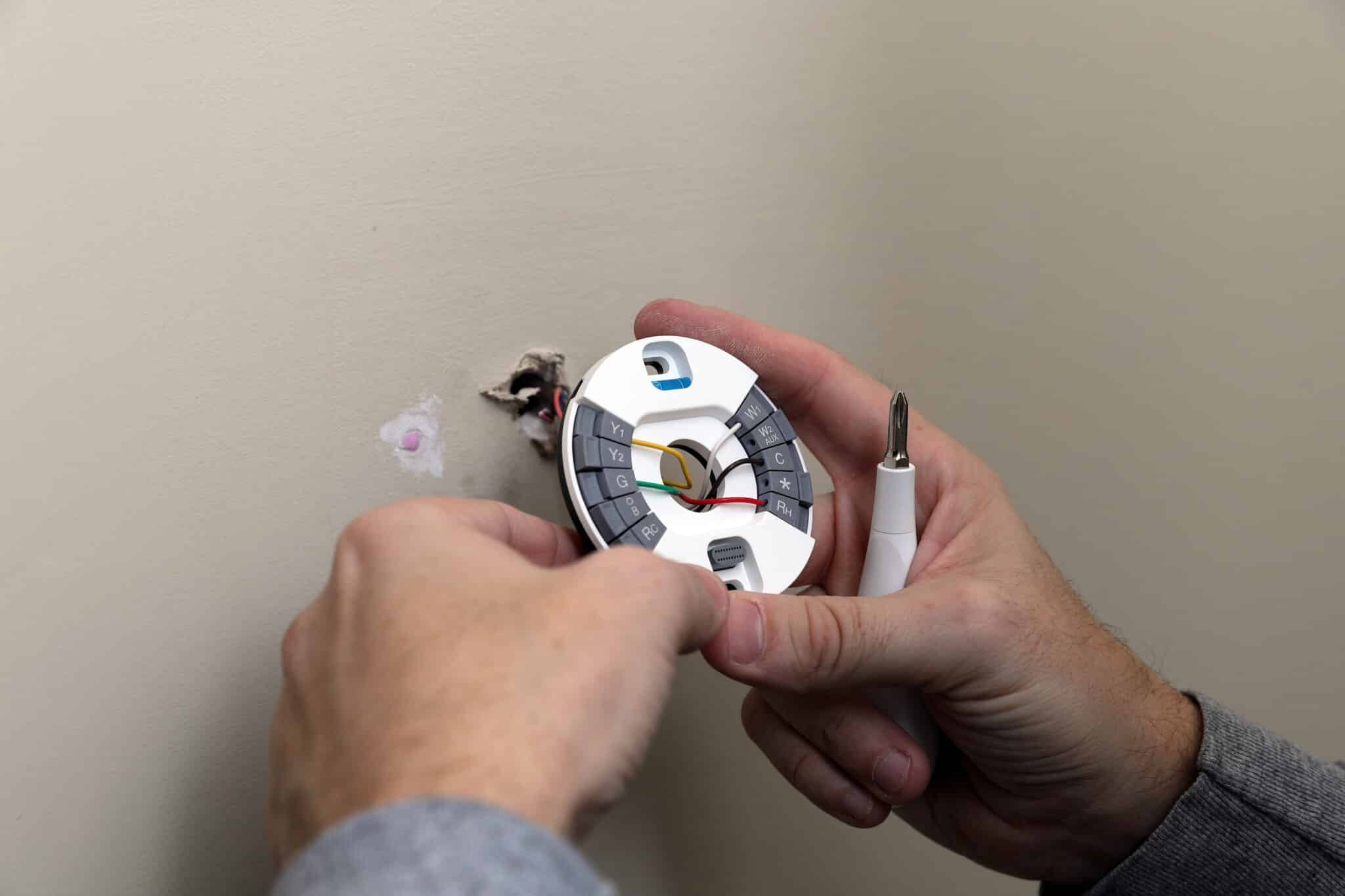 Hand installing thermostat plate on wall, Temperature Zoning.