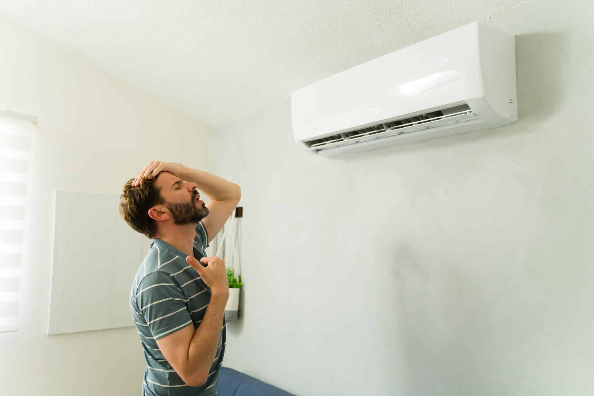 Stressed man suffering hot weather feeling frustrated by broken air conditioner unit, Outdated HVAC.