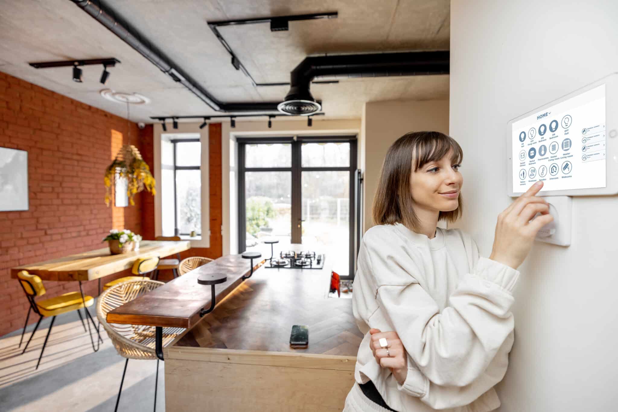 Young pretty woman controlling smart home devices with a digital tablet mounted on the wall. Wide angle view on stylish living room interior, Ventilation Optimization.